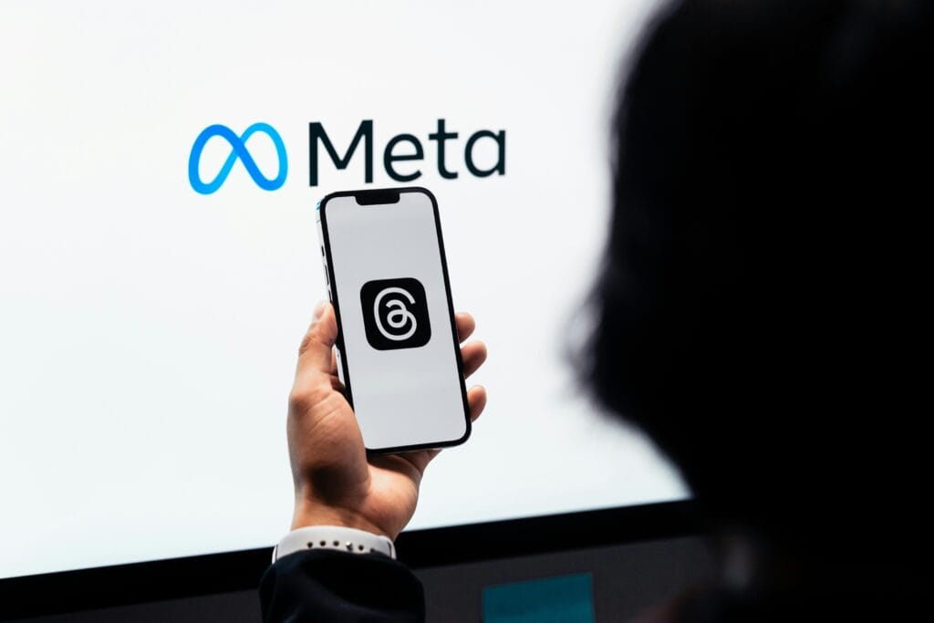 Meta introduz IA para criar perfis no Facebook e Instagram 1 Hands holding smartphone with Meta Threads logo on screen, Meta branding in background.