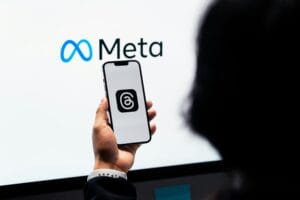 Meta introduz IA para criar perfis no Facebook e Instagram 6 Hands holding smartphone with Meta Threads logo on screen, Meta branding in background.
