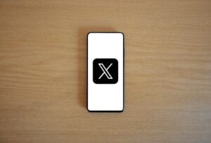 Recupere sua conta suspensa no X (Twitter) facilmente 5 Minimalist image of smartphone with X logo on wooden surface, showcasing digital branding.