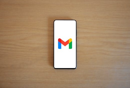 Google AI: A Revolução da Inteligência Artificial Chegou ao Gmail, Docs, Sheets, Meet, Chat e Slides 3 A smartphone displaying the Gmail app logo on a wooden surface, viewed from above.